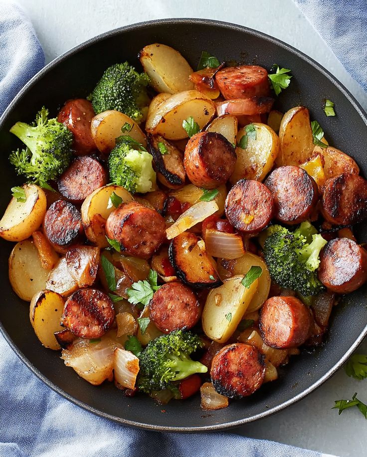 a pan filled with sausage, potatoes and broccoli on top of a blue towel