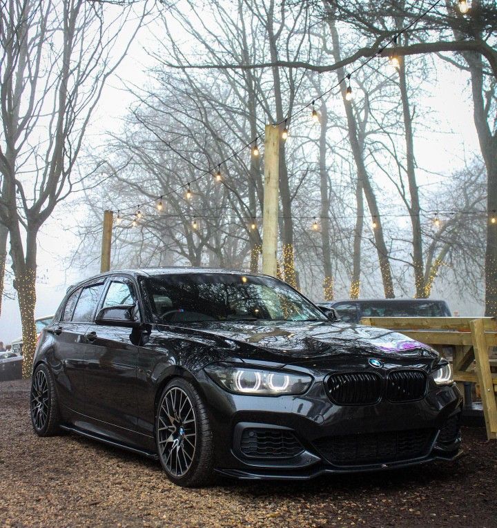 a black car parked next to a picnic table with lights strung from the trees behind it