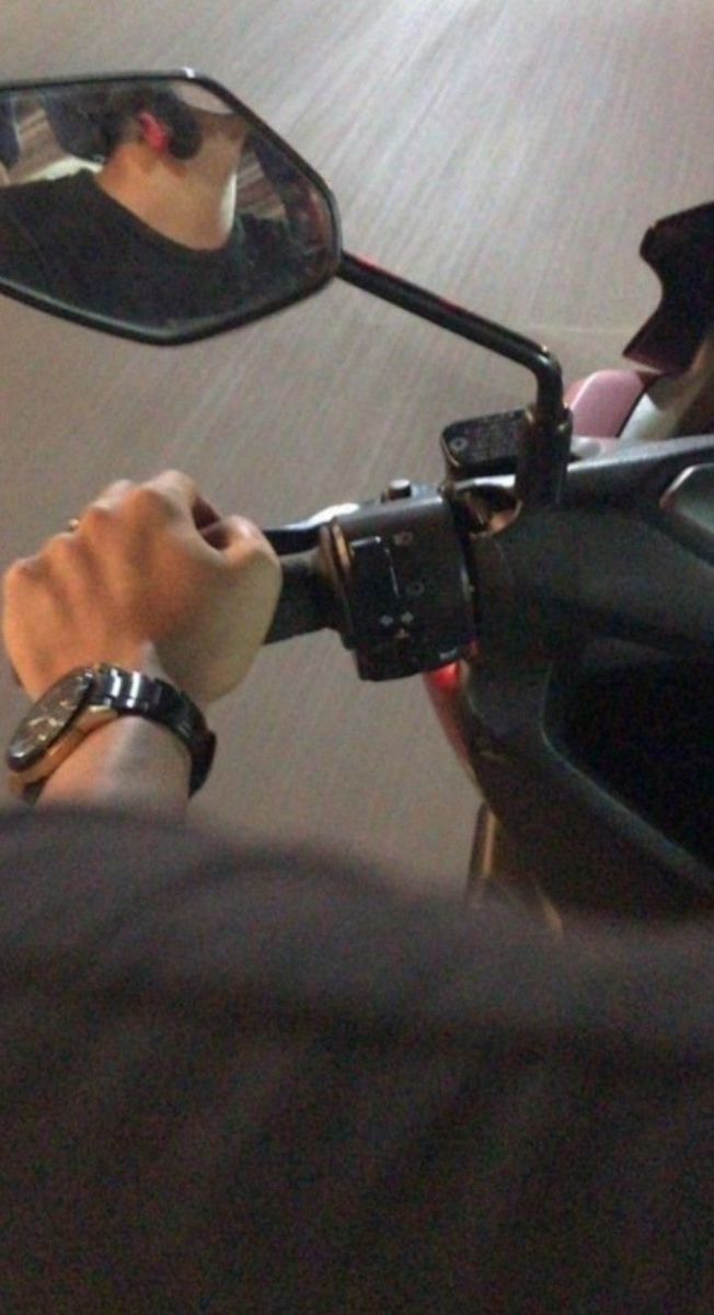 a man driving a motorcycle down a street next to a person with a wrist watch