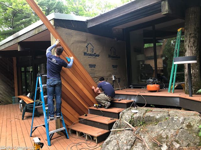 two men working on the side of a house with wooden stairs and steps leading up to it