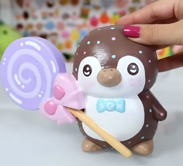 a hand is holding a toy penguin with a lollipop