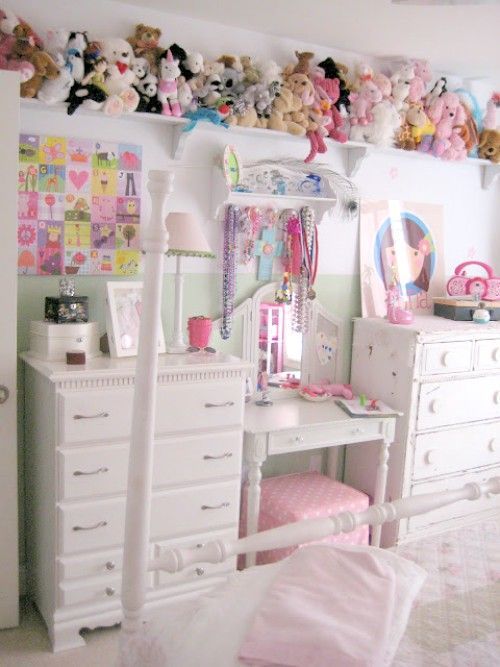 a bedroom with white furniture and lots of stuffed animals on the wall above it's desk