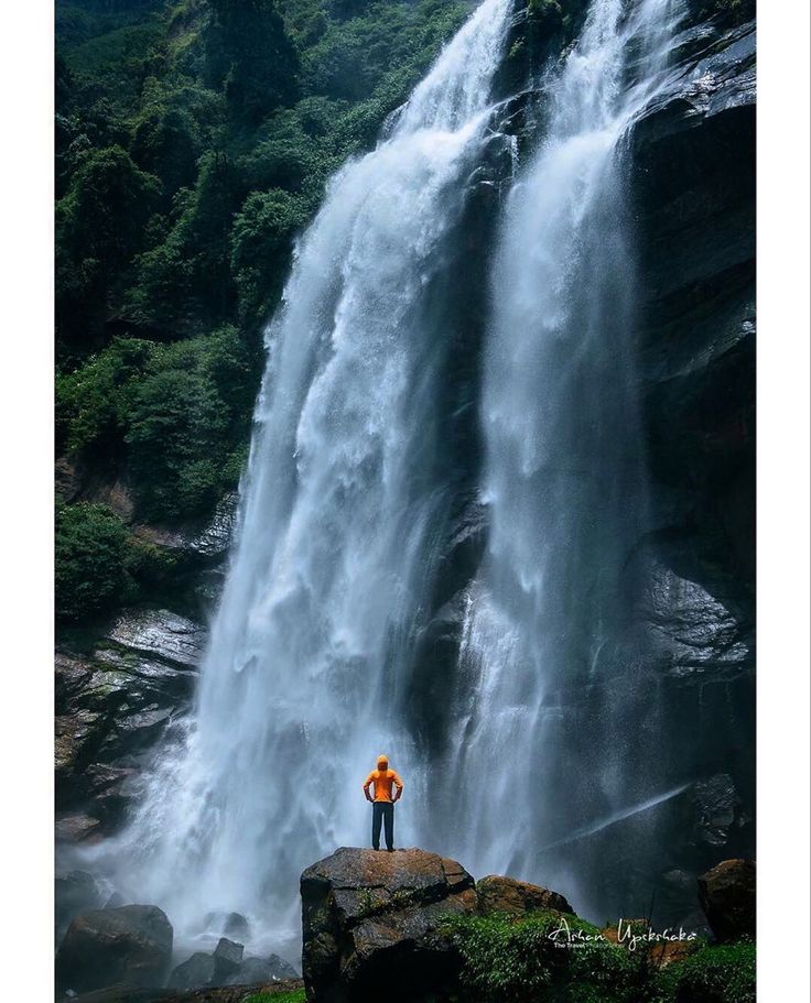 a man standing in front of a large waterfall