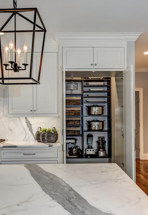 a kitchen with white cabinets and marble counter tops, an island in the middle is surrounded by hanging lights