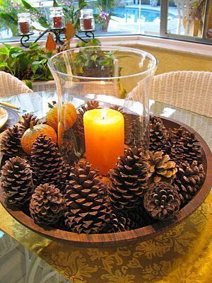 a candle is lit in a bowl with pine cones around it on a dining room table