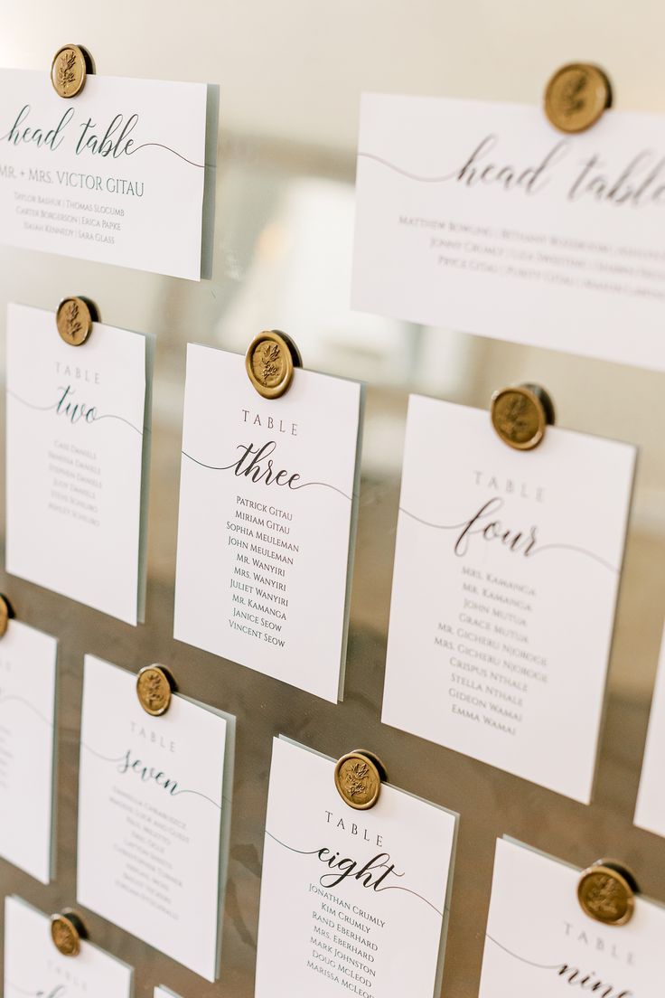 wedding seating cards with gold buttons attached to the back of each place card, hanging on a wall