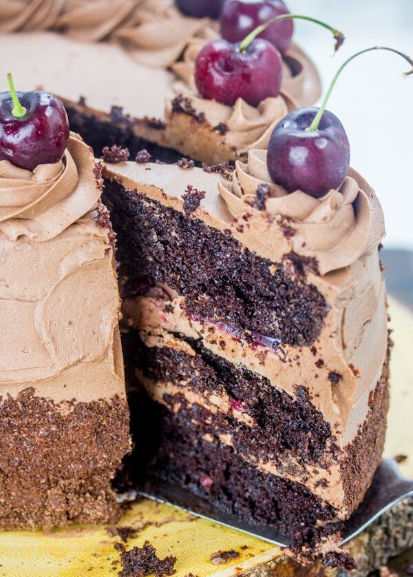 a cake with chocolate frosting and cherries is cut from the side on a plate