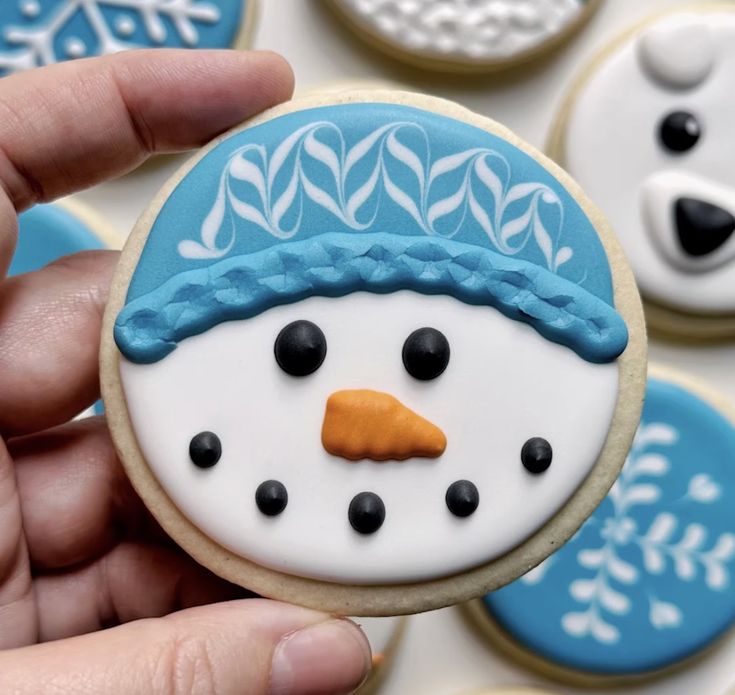 a hand holding a decorated cookie with frosting on it and an image of a snowman