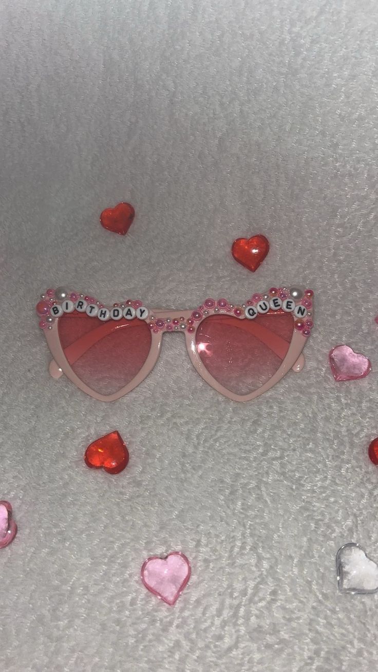 a pair of heart shaped sunglasses sitting on top of a white surface with hearts scattered around it