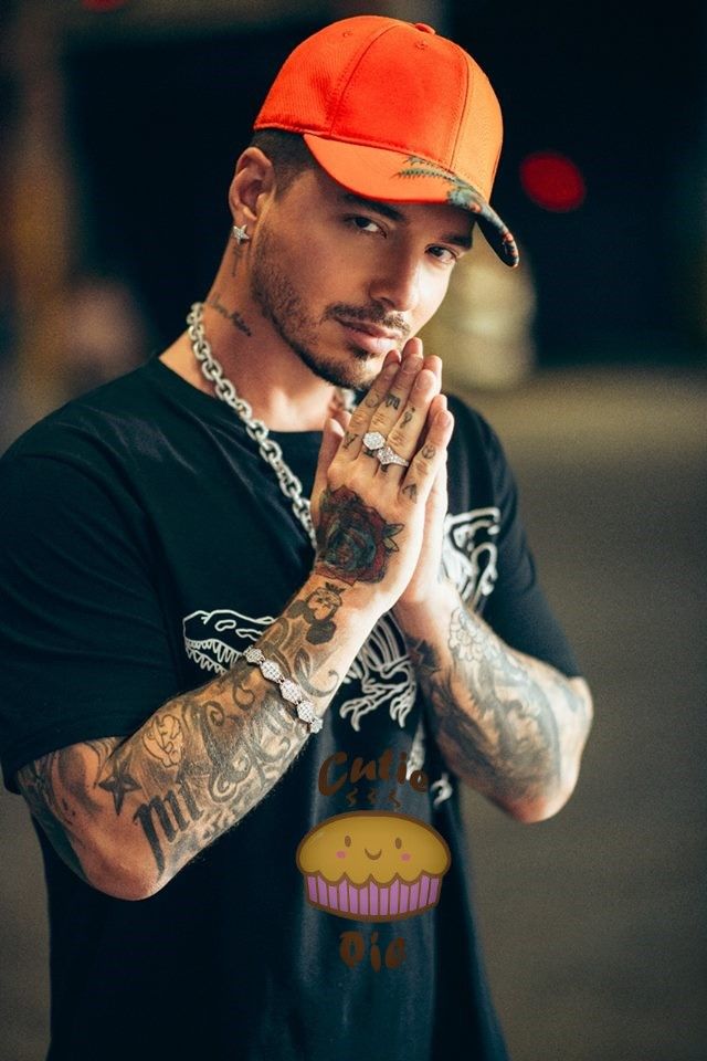 a man with tattoos and an orange hat is holding his hands to his face while standing in the street