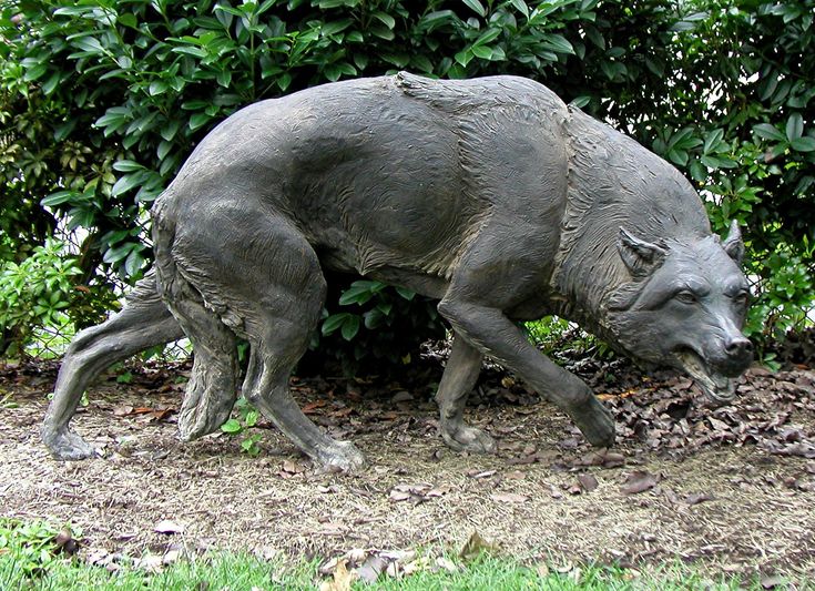 a statue of a wolf walking in front of bushes