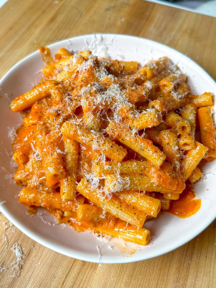 a white plate topped with pasta covered in parmesan cheese on top of a wooden table