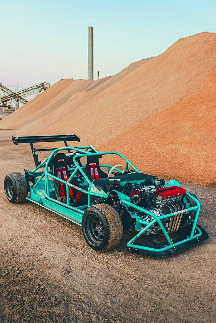 a blue race car sitting on top of a dirt road next to a pile of sand