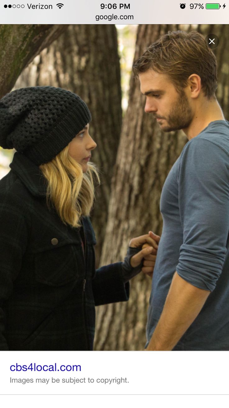 a man and woman standing next to each other in front of some trees, talking