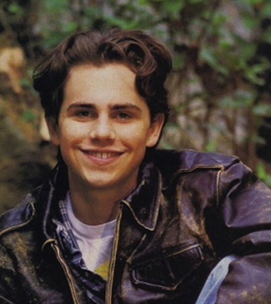 a young man in a leather jacket is holding a knife and smiling at the camera