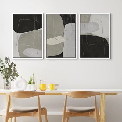 three paintings hang on the wall above a dining room table with two chairs and a vase