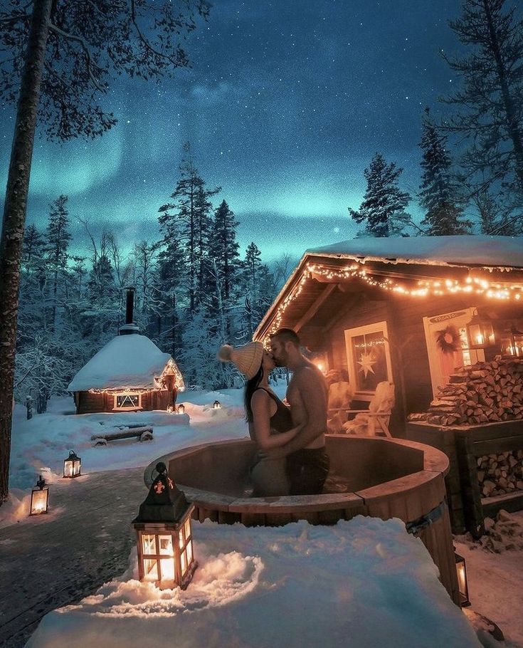 a woman sitting in a hot tub next to a cabin at night with lights on