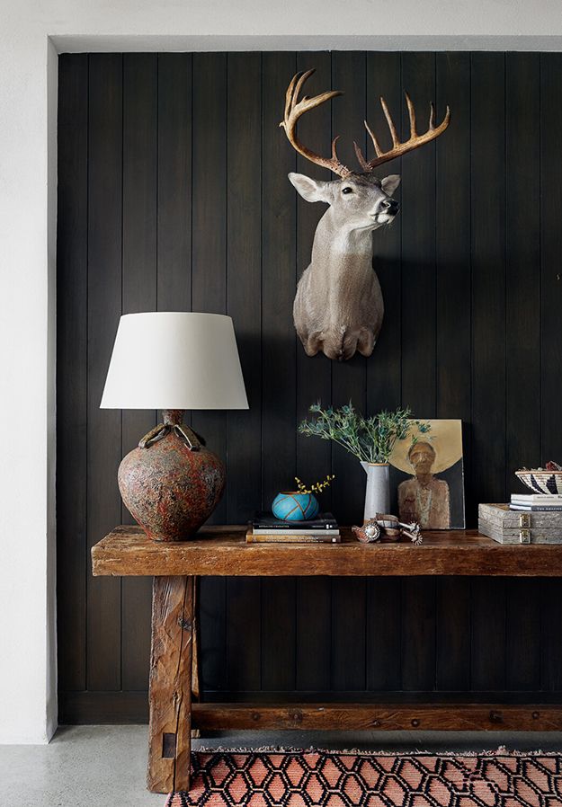 a deer head mounted on the wall above a wooden table with vases and lamps