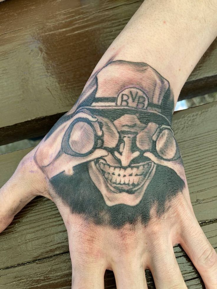 a man's hand with a skull wearing a hat and goggles on it