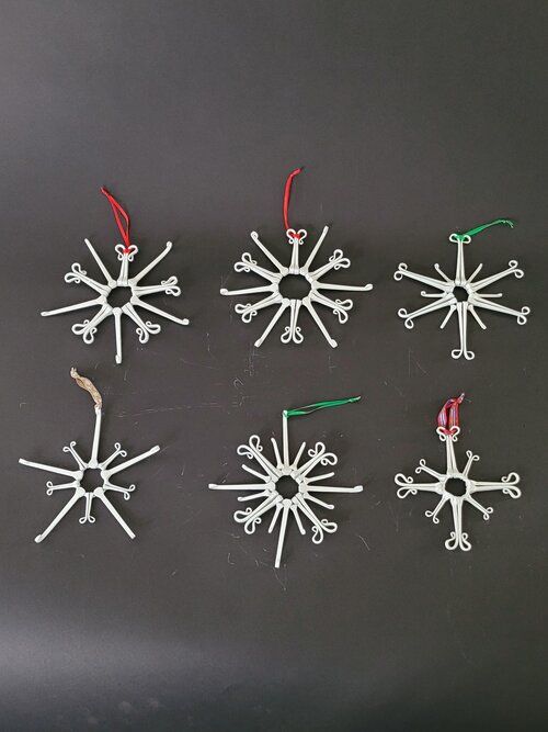 six snowflakes are hanging from strings on a black surface with red and green string