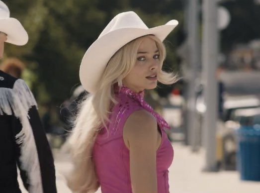 two people in cowboy hats are walking down the street together, one is wearing a pink dress and the other has a white hat