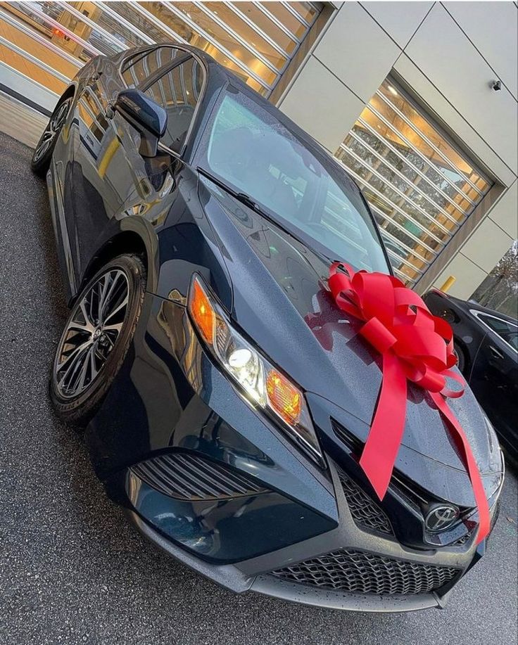 a black car with a red bow on it's hood parked in front of a building