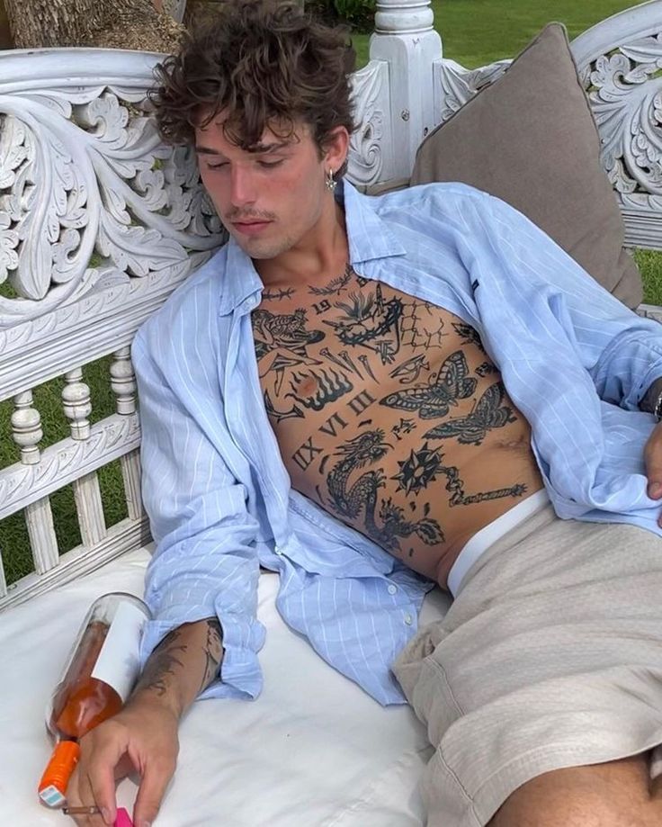 a man with tattoos sitting on a white bench holding a bottle and an orange object