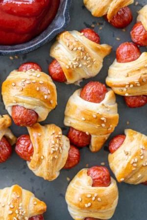 pigs in a blanket wrapped in bread and topped with strawberries next to a bowl of ketchup