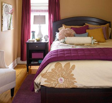 a bed with purple and yellow pillows in a bedroom next to a lamp on a table