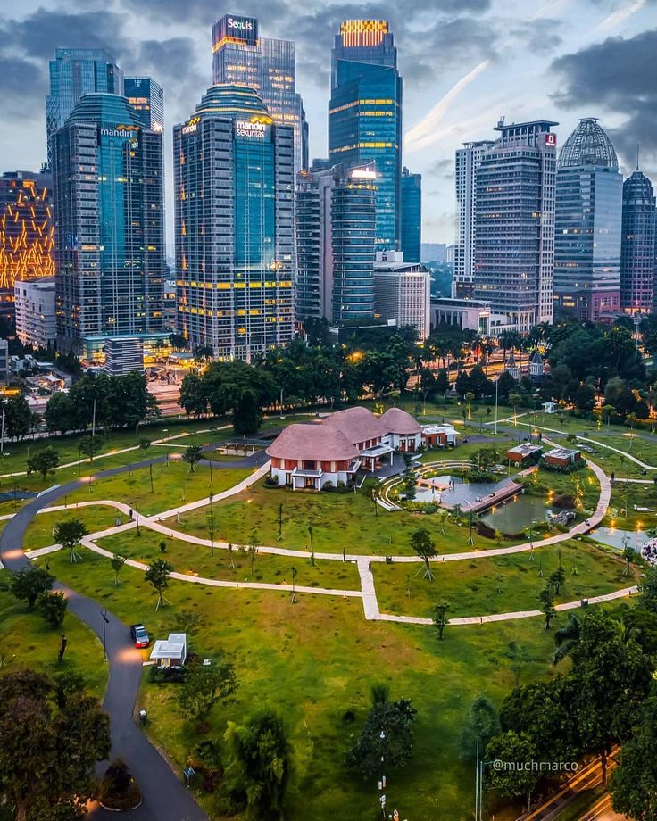 an aerial view of a park in the middle of a city with tall buildings behind it