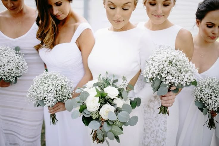 a group of women standing next to each other holding bouquets filled with white flowers