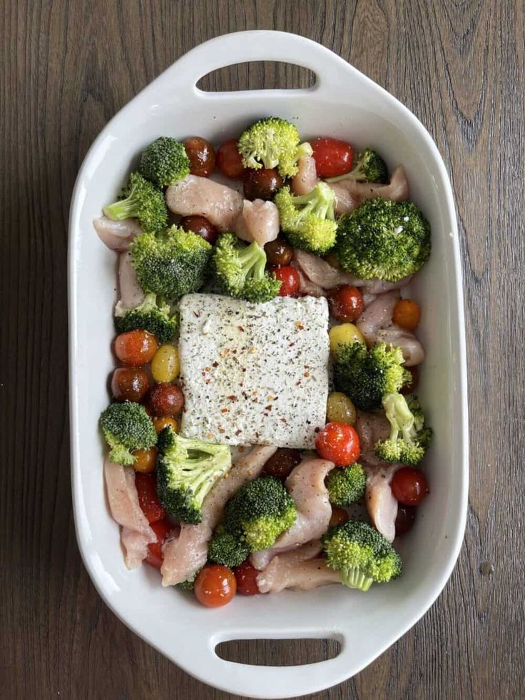 a white dish filled with broccoli, tomatoes and chicken