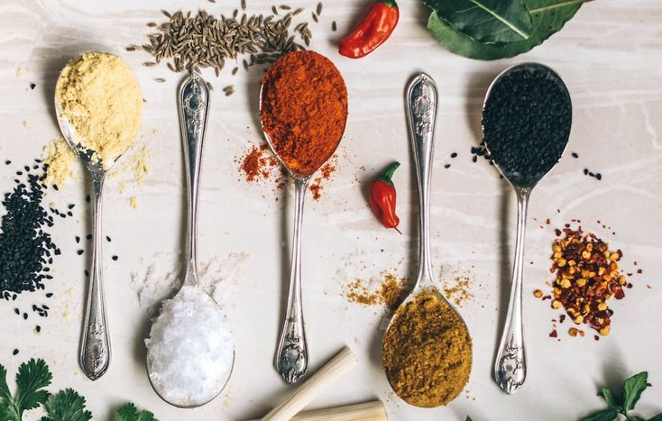 five spoons with different types of spices and herbs next to them on a table