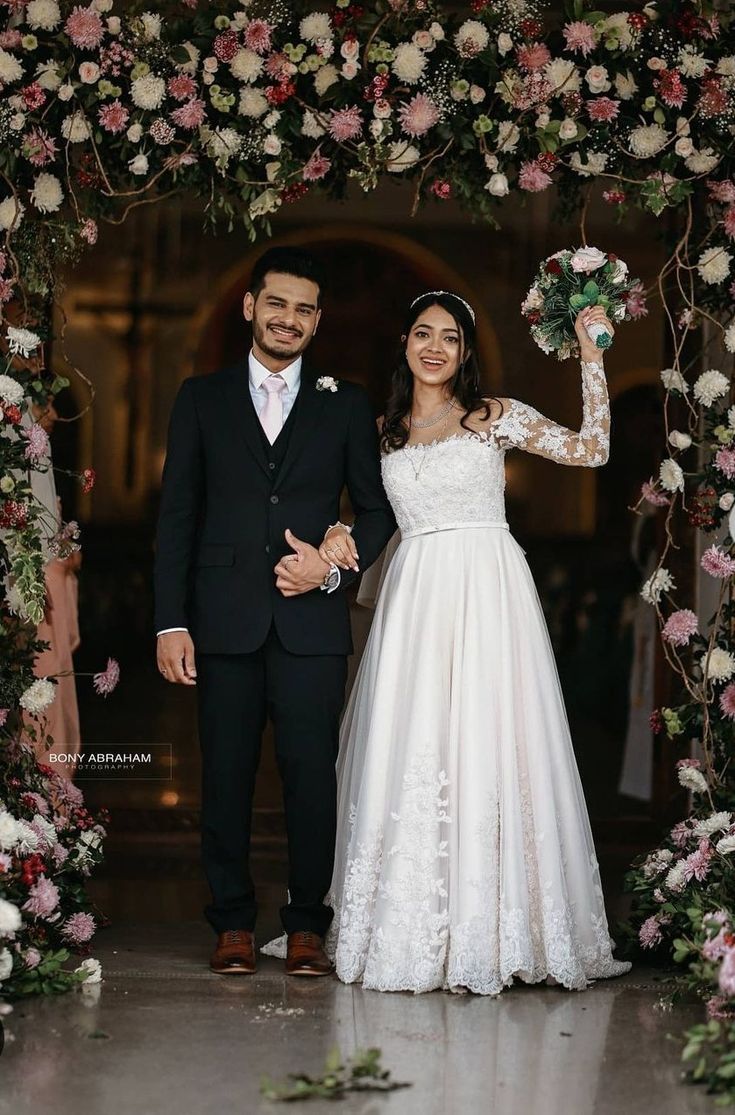 a bride and groom standing in front of a floral arch