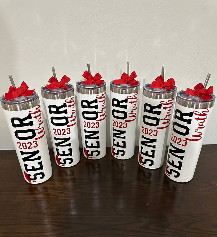 six personalized travel tumbles with red bows on the top and bottom, sitting on a table