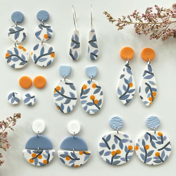 several pairs of blue and orange earrings on a white surface next to some dried flowers