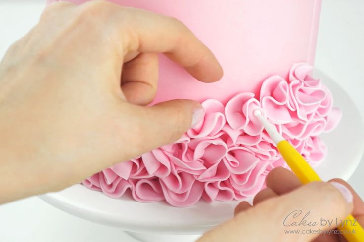 someone is decorating a pink cake with ruffles and a yellow marker on it