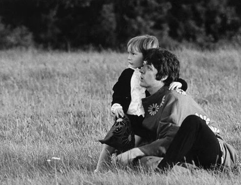 black and white photograph of two people sitting in the grass with one holding a child