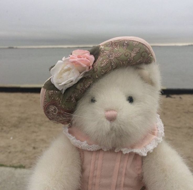 a white teddy bear wearing a pink dress and hat with flowers on it's head