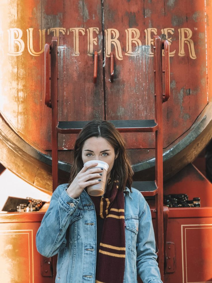 a woman drinking from a coffee cup in front of a barrel with the word butterbeeer on it