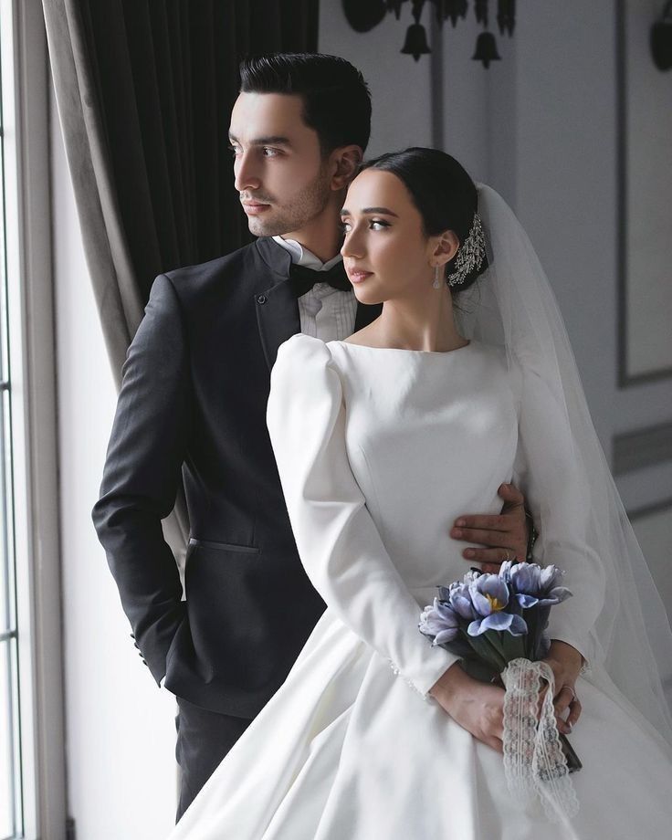 a man and woman in wedding attire standing next to each other with their arms around each other