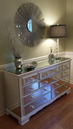 a silver dresser sitting in front of a mirror on top of a wooden floor next to a lamp