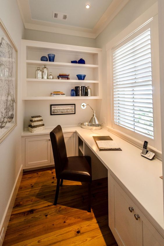 a home office with white walls and wooden flooring, built - in shelving