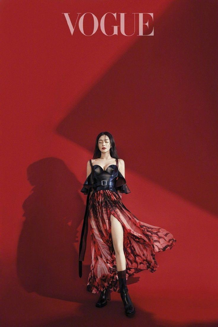 a woman standing in front of a red wall wearing a black dress and high heels