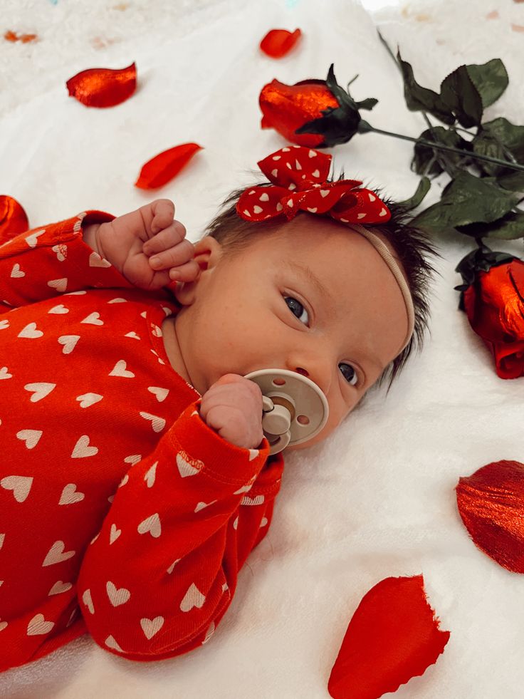 a baby with a pacifier in it's mouth laying next to rose petals