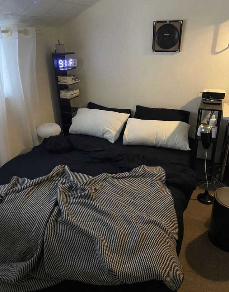 a bed with black sheets and white pillows in a room next to a clock on the wall