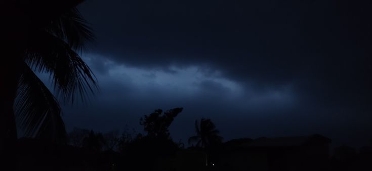 a dark sky with clouds and trees in the foreground