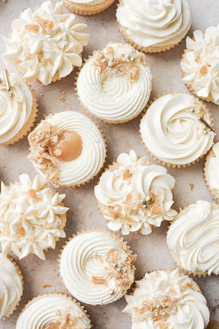 cupcakes with white frosting and sprinkles are arranged on a baking sheet