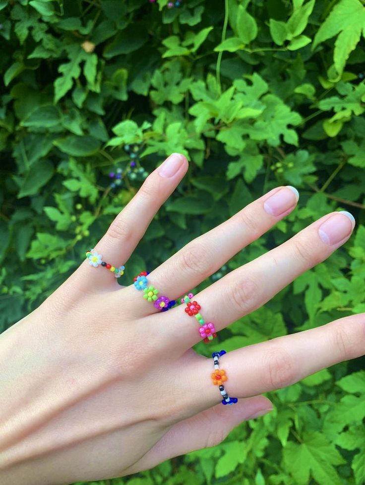 a woman's hand with multicolored beaded rings on her fingers and green leaves in the background