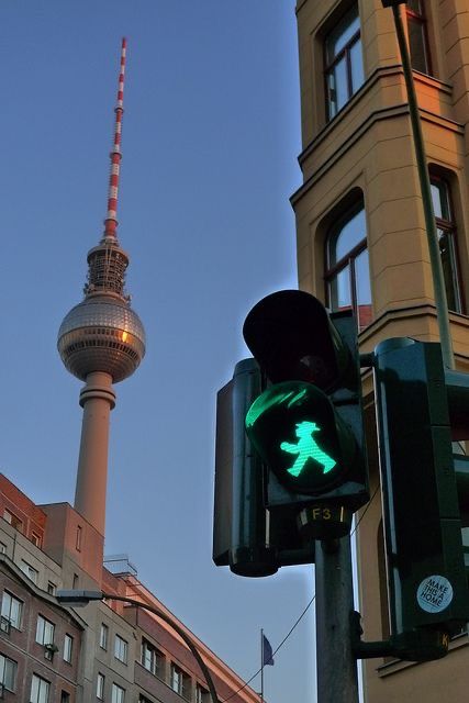 a traffic light with a green pedestrian crossing signal in the foreground and a television tower in the background